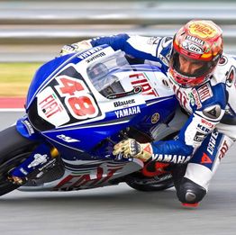 Motorcyclist in blue and white racing gear leaning into a sharp turn on a track.