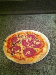 Pizza mit Salami, Pilzen und Käse auf einem weißen Teller, auf einer granitenen Oberfläche.