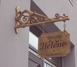 Antikes Schild mit Aufschrift "Fräulein Helene - Für alle Zeiten", an einer Hauswand befestigt.