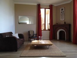 Salon moderne avec canapé marron, table basse en bois et cheminée, décoré de rideaux rouges.