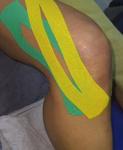 Rodilla con cintas kinesiológicas verde y amarilla aplicadas sobre la piel.