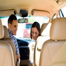 Two people smiling in a car, looking back at the camera from the front seats.