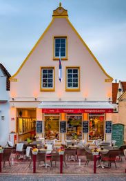 Gelbes Café mit Terrasse, Tischen und Stühlen; blauer Himmel im Hintergrund.