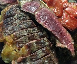 Carne asada en rodajas, con trozos de tomate rojo a un lado, servida en un plato negro.