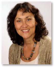 Porträt einer lächelnden Frau mit lockigem Haar und einer Halskette vor neutralem Hintergrund.