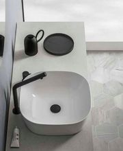 Lavabo moderno con rubinetto nero, piastrelle esagonali e accessori neri su piano chiaro.