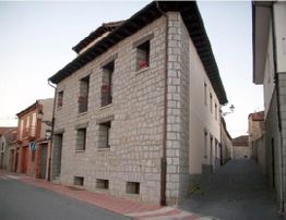 Edificio de piedra en esquina de calle con ventanas y cielo despejado.