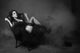 Elegant woman in black dress reclines in a smoky room, striking a dramatic pose.