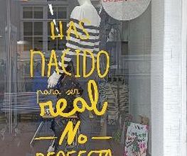 Escaparate con frase: "Has nacido para ser real, no perfecta". Ropa y cartel "Nueva Colección".