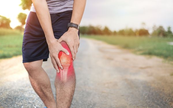 Ein Jogger hält sich das Knie, welches grafisch rot markiert wurde, um den Schmerz zu symbolisieren.