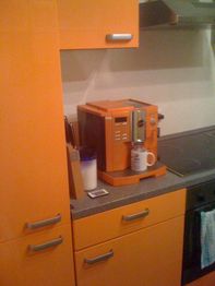 Orange Küche mit passender Kaffeemaschine, Messern, Tasse und einem Deckel auf der Arbeitsplatte.