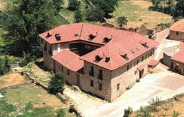 Imagen aérea de un gran edificio de piedra con techo rojo, rodeado de vegetación y caminos.
