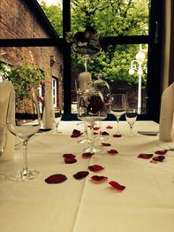 Elegante Tischdekoration mit Gläsern, roten Rosenblättern und Blick nach draußen.