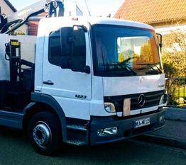 Weißer Lastwagen mit Kranarm, geparkt vor Wohnhäusern. Nummernschild NE-AH 1123.