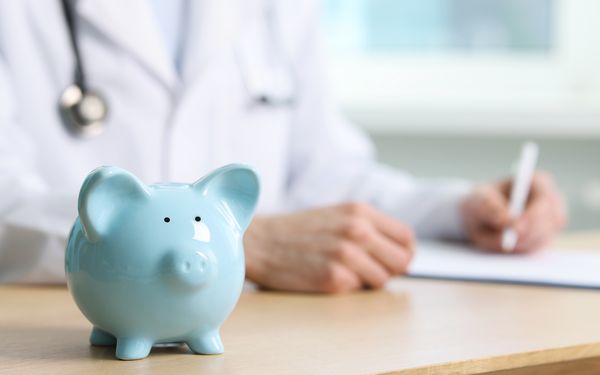 Sparschwein im Vordergrund, während eine medizinische Fachkraft im Hintergrund Unterlagen ausfüllt.