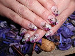 Dekorierte Fingernägel mit Schmetterlingsmotiven auf violetten Blütenblättern.