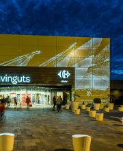 Entrada iluminada de un centro comercial por la noche, con letrero de bienvenida en catalán.