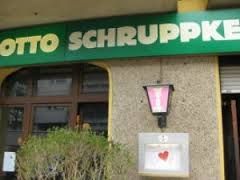 Ladenschild "OTTO SCHRUPPKE" auf grünem Hintergrund, mit Laterne und Herz-Symbol darunter.