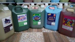 Galões de produtos de limpeza coloridos alinhados sobre um piso de madeira e pedra.