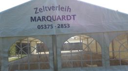 Ein weißes Zelt mit der Aufschrift "Zeltverleih MARQUARDT 05375-2853" über dem Eingang.