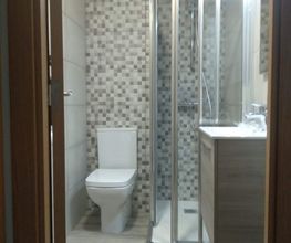 Baño moderno con ducha de vidrio, inodoro, lavabo y pared de azulejos grises y blancos.