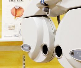 Equipo de optometría con gráfico ocular de fondo en una sala de examen visual.
