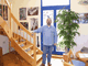 Mann steht neben Treppe in einem hellen Raum mit Pflanzen und Fotos an der Wand.