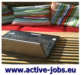 Laptop auf Holztisch mit bunten Kissen im Hintergrund. Unten steht: www.active-jobs.eu.