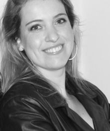 Mulher sorrindo, cabelo claro e casaco escuro, em foto preto e branco.