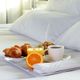 Breakfast tray on a bed with croissants, juice, coffee, and an orange slice.
