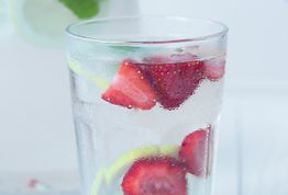 Glas mit Wasser, Zitronenscheiben und Erdbeeren; erfrischendes Getränk auf weißem Hintergrund.