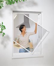 Frau öffnet ein Fenster mit quadratischem Rahmen; im Hintergrund eine Küche sichtbar.