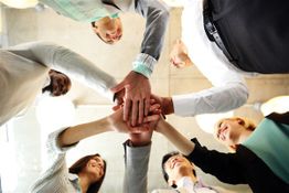 A group of people standing in a circle with their hands stacked together, viewed from below.