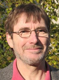 Mann mit Brille lächelt, Hintergrund aus grünem Laub.