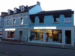 Zwei blau gestrichene Häuser mit Schildern, auf denen "MonDe" und Fenster mit Inneneinrichtung.