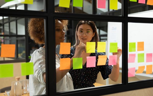 Zwei Arbeitskolleginnen organisieren ihre Arbeitsstrucktur mit verschieden farbigen Post-Its.