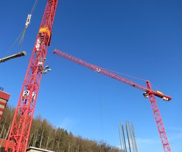 Zwei rote Baukräne heben Baumaterial in den blauen Himmel über einer Baustelle.