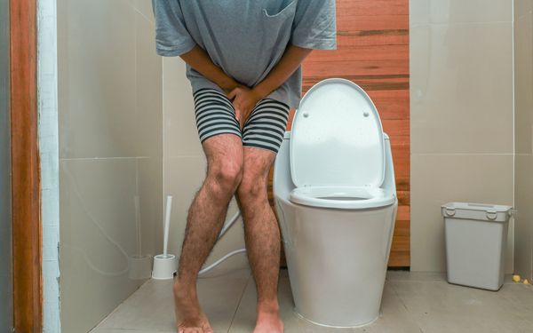 Mann mit Harndrang steht vor einer Toilette und hält sich den Unterbauch.