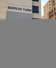 Edificio Turis con ventanas y otro edificio cercano bajo un cielo azul claro.