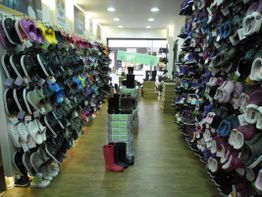 Schuhgeschäft mit zwei Reihen von Crocs und anderen Schuhen, rote Stiefel in der Mitte.