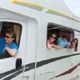 People leaning out of an RV's windows, smiling and wearing sunglasses.