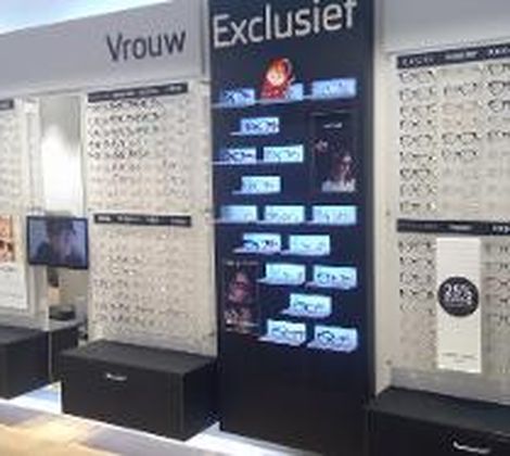 Wand met brillen op displays, onderverdeeld in "Vrouw" en "Exclusief". Diverse stijlen en prijzen.