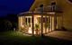 Beleuchteter Wintergarten an einem Haus bei Nacht mit Blick auf den Garten.