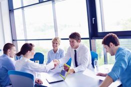 Business meeting with people shaking hands in a bright office with large windows.
