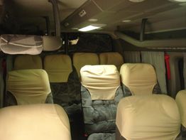 Interior de uma van com bancos cobertos por capas bege, dispostos em fileiras duplas.