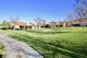 Pathway through a grassy park with buildings and trees under a clear blue sky.