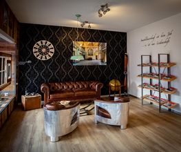 Gemütliches Wohnzimmer mit Ledersofa, Wanduhr, Wandbild, und Bücherregal auf Holzboden.