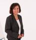 Eine lächelnde Frau in einem dunklen Blazer steht vor einem weißen Hintergrund.