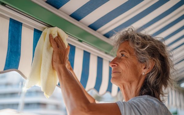 Frau reinigt eine blau-weiß-gestreifte Markise mit einem weichen hellen Lappen.