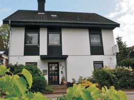 Zweistöckiges weißes Haus mit dunkler Verkleidung und gepflegtem Garten im Vordergrund.